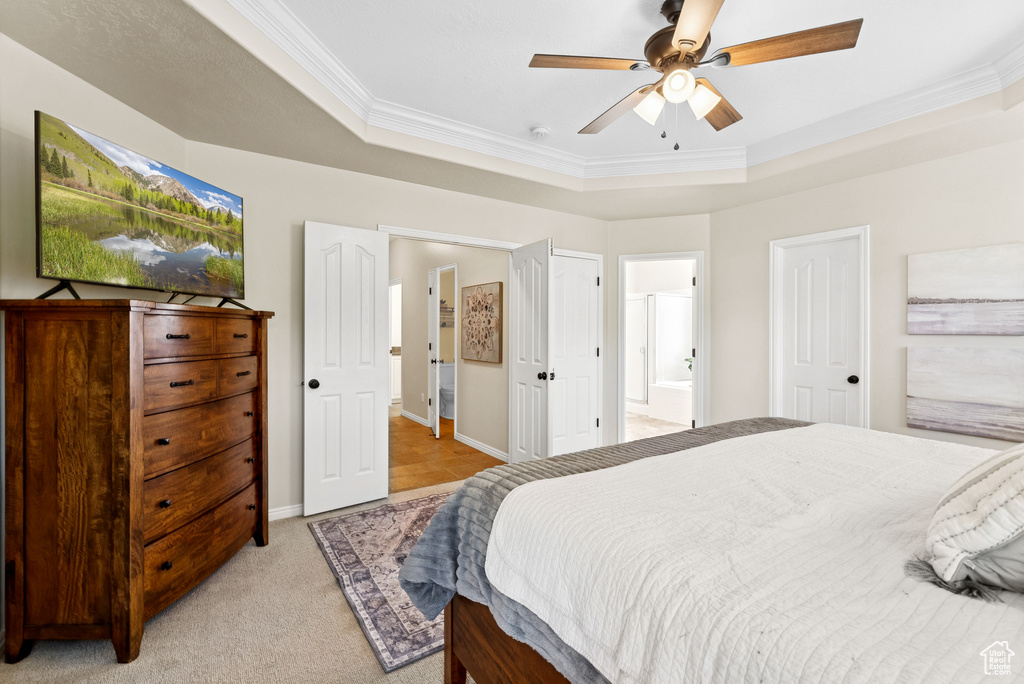 Bedroom featuring ornamental molding, a raised ceiling, light colored carpet, connected bathroom, and ceiling fan