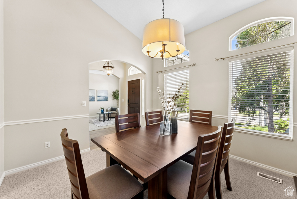 Carpeted dining area featuring arched walkways, a chandelier, and high vaulted ceiling