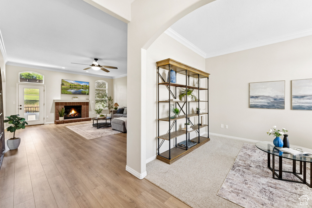 Sitting room with crown molding, a ceiling fan, arched walkways, a brick fireplace, and wood finished floors