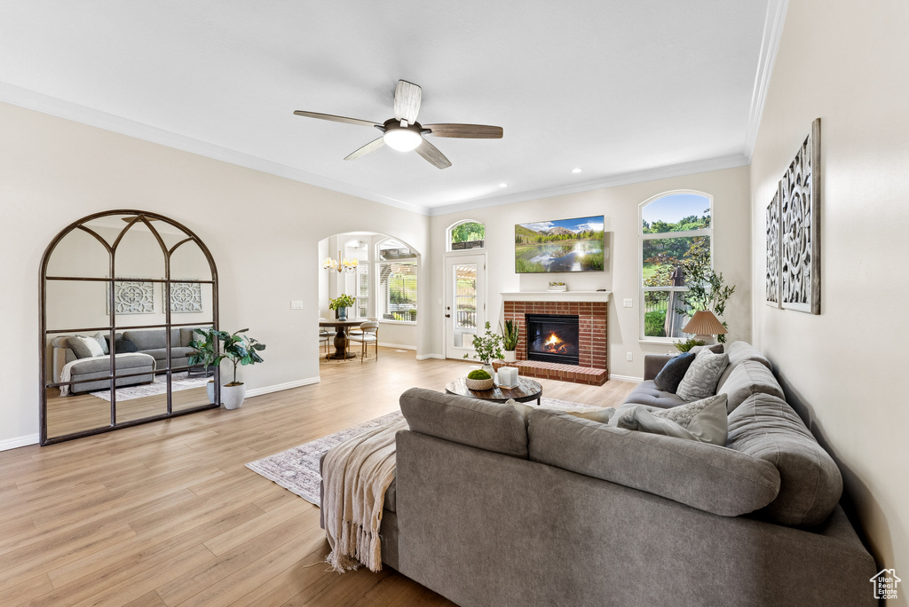 Living area featuring arched walkways, crown molding, a ceiling fan, light wood finished floors, and a fireplace
