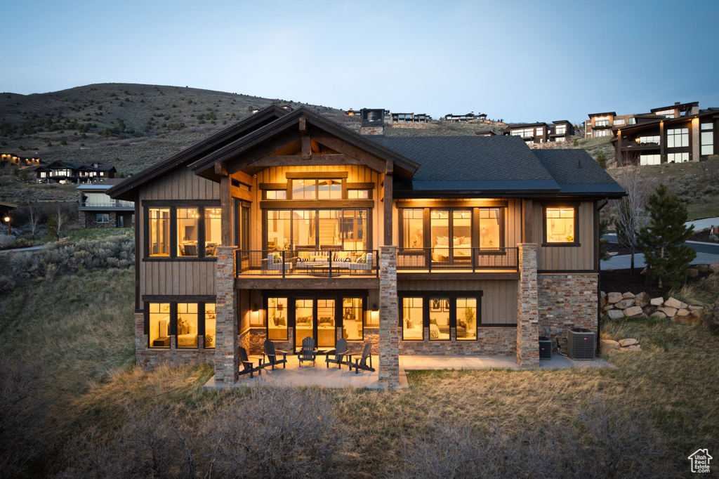 Back of property featuring a patio, stone siding, a mountain view, board and batten siding, and a shingled roof