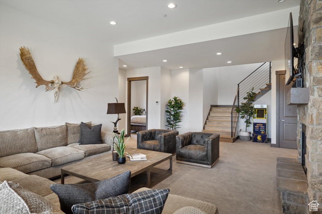 Living area with a stone fireplace, stairway, light carpet, and recessed lighting