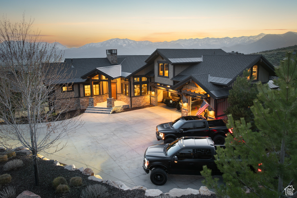 Back of property at dusk with a mountain view, driveway, a chimney, and stone siding