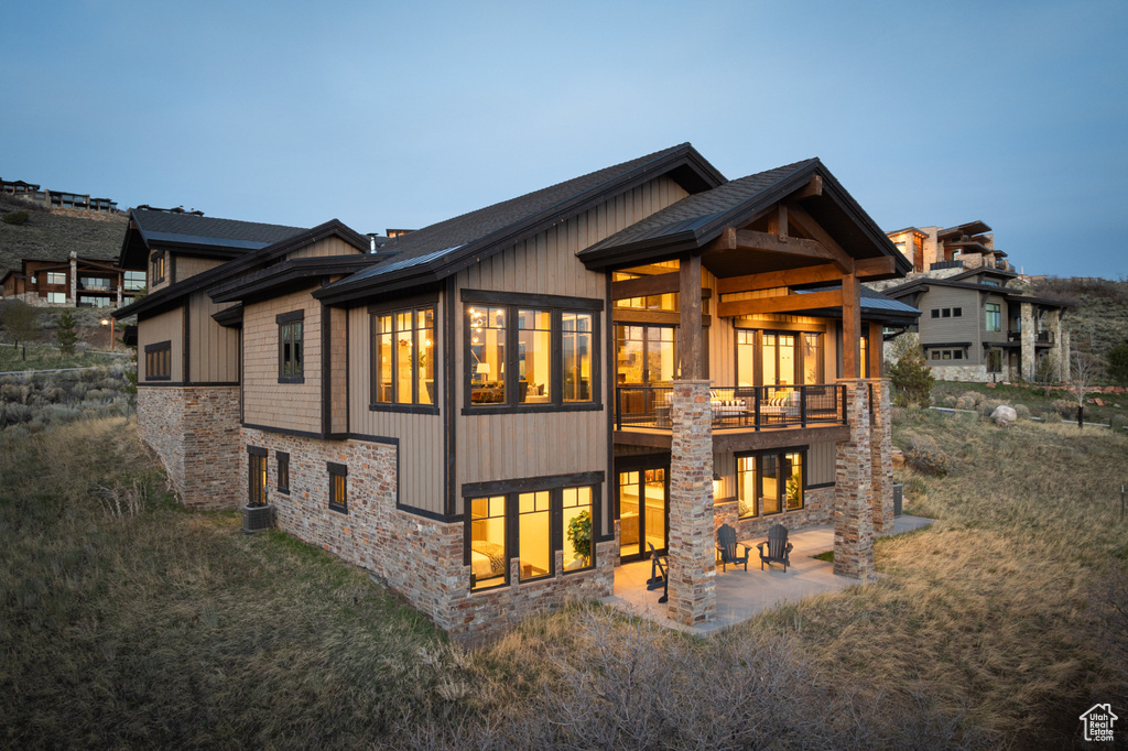 Back of property with stone siding, a patio, and a shingled roof