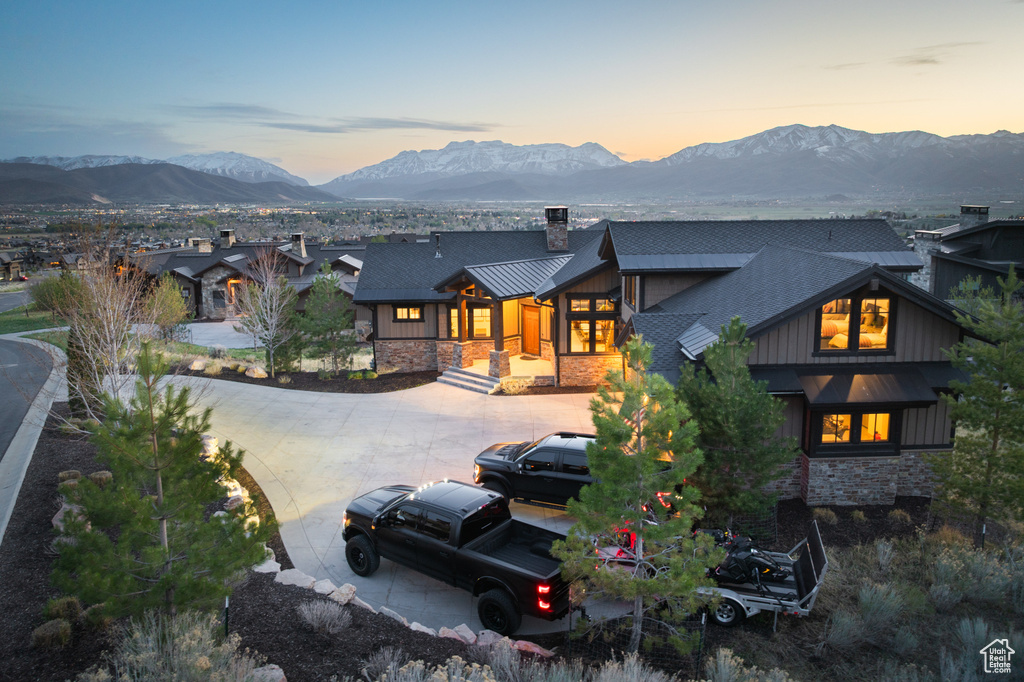 Back of property at dusk with stone siding, a chimney, a mountain view, a standing seam roof, and board and batten siding
