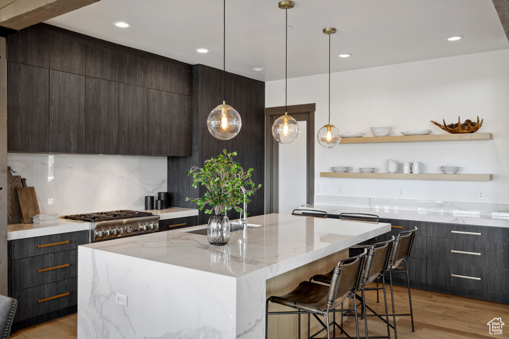 Kitchen featuring modern cabinets, dark brown cabinets, light wood finished floors, light stone countertops, and recessed lighting