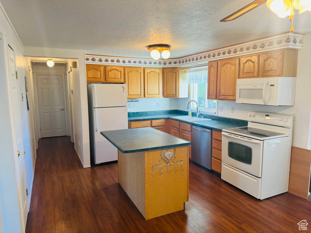 Kitchen featuring white appliances, dark wood-type flooring, dark countertops, a textured ceiling, and a kitchen island