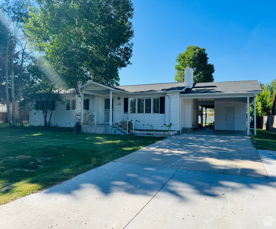 Single story home with driveway, a front yard, a chimney, a carport, and roof with shingles