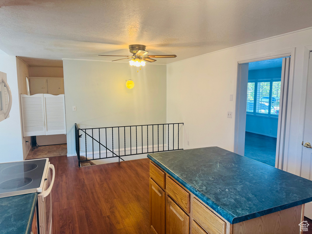 Kitchen featuring electric range, a ceiling fan, dark wood finished floors, dark countertops, and a kitchen island