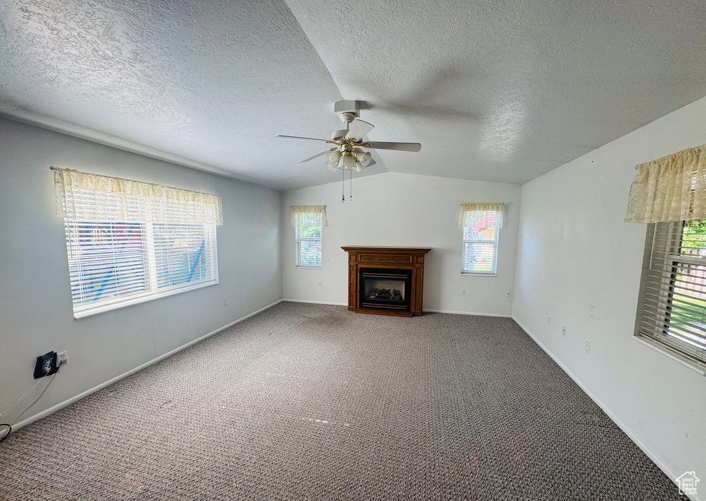 Unfurnished living room with a ceiling fan, vaulted ceiling, healthy amount of natural light, a fireplace, and carpet