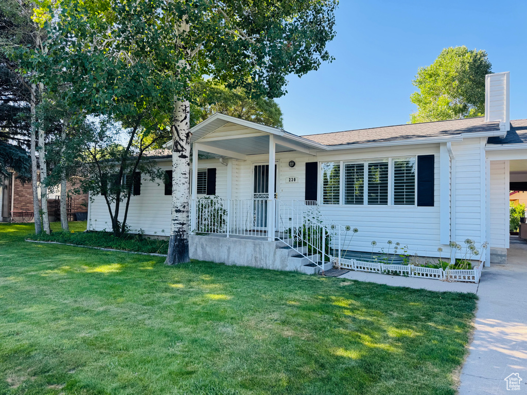 View of front facade featuring a front yard, an attached carport, covered porch, concrete driveway, and a chimney