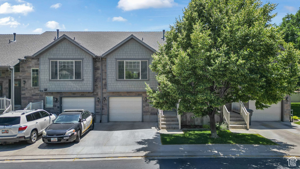 Townhome / multi-family property with driveway, an attached garage, roof with shingles, and stone siding