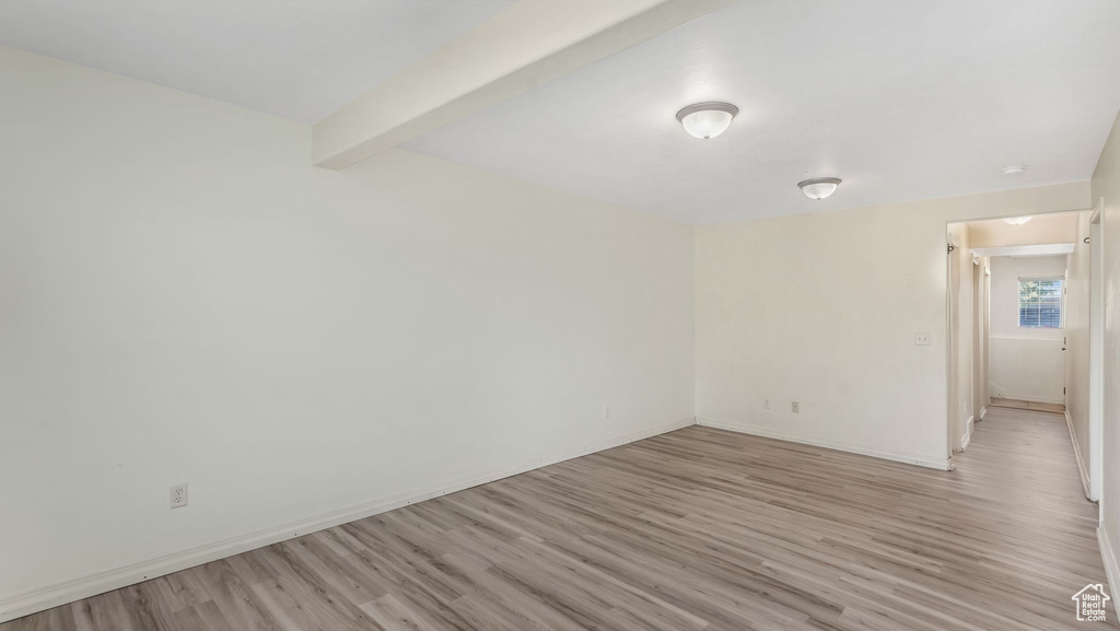 Empty room with light wood-style floors and beam ceiling