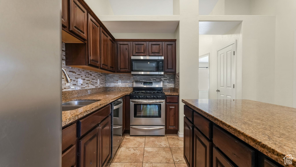 Kitchen featuring appliances with stainless steel finishes, tasteful backsplash, dark brown cabinetry, and stone countertops