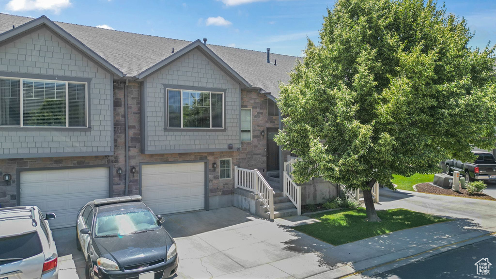 View of property featuring driveway, stone siding, a shingled roof, and an attached garage