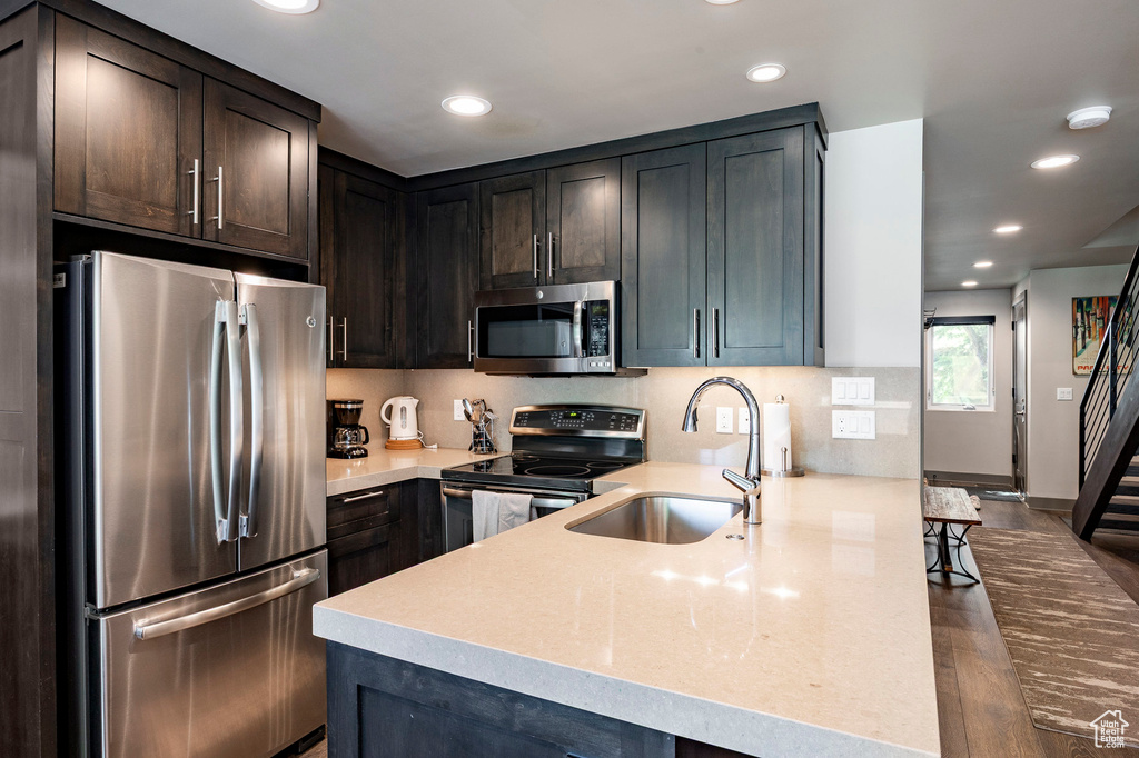 Kitchen with stainless steel appliances, a peninsula, recessed lighting, dark wood-type flooring, and dark brown cabinetry
