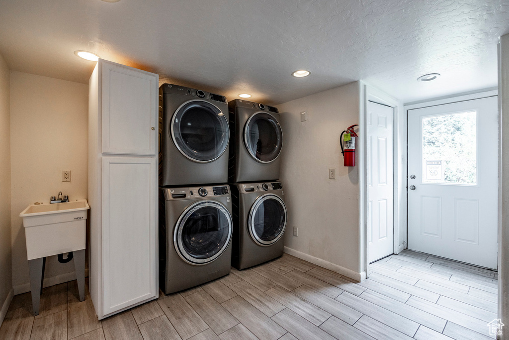 Laundry area with stacked washer and clothes dryer, wood tiled floors, washer and dryer, cabinet space, and a textured ceiling