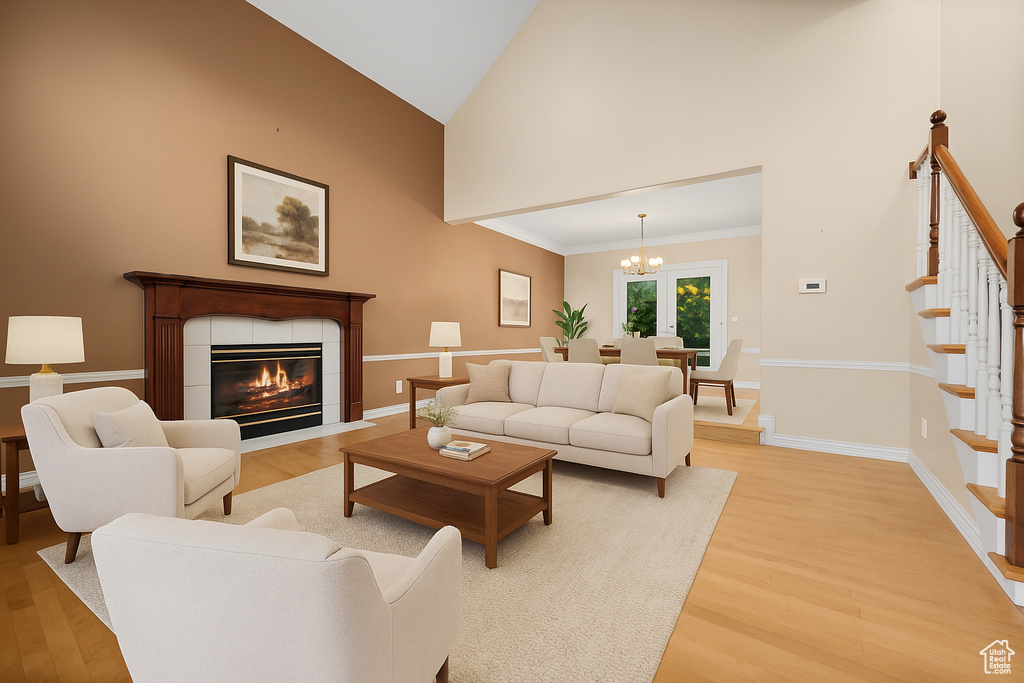 Living room with light wood finished floors, stairway, high vaulted ceiling, a chandelier, and a tiled fireplace