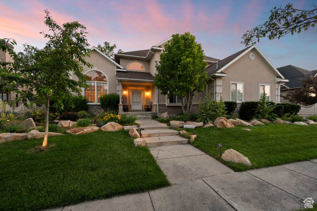 View of front facade featuring stucco siding, a lawn, and stone siding