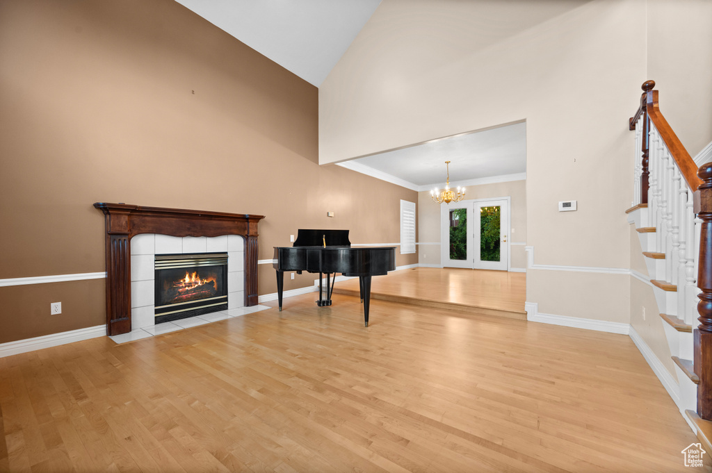 Unfurnished living room featuring high vaulted ceiling, light wood-style floors, stairway, a tile fireplace, and french doors
