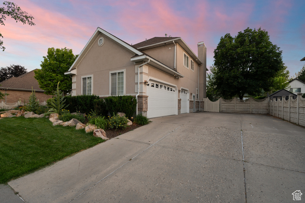 Property exterior at dusk featuring concrete driveway, stucco siding, a chimney, and a garage