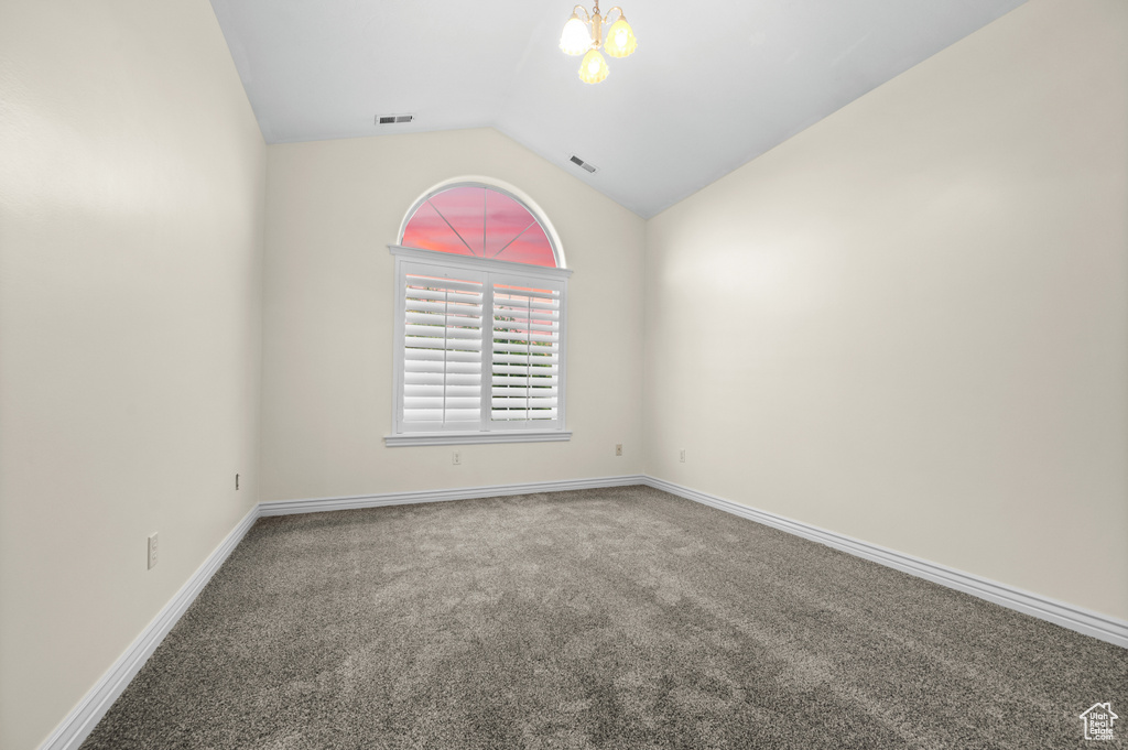 Carpeted empty room featuring vaulted ceiling and a chandelier