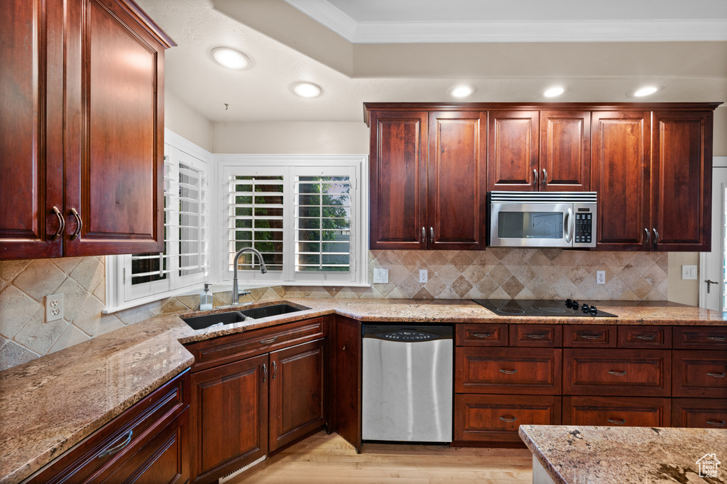 Kitchen with appliances with stainless steel finishes, light stone countertops, ornamental molding, tasteful backsplash, and light wood-style floors