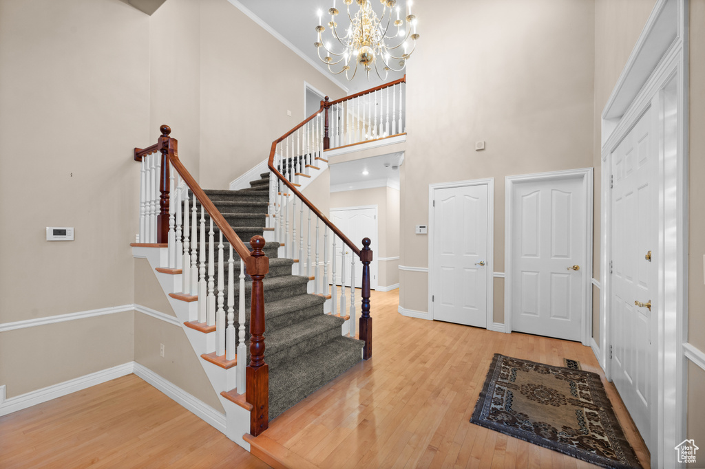 Entryway featuring wood finished floors, a towering ceiling, stairs, a chandelier, and crown molding