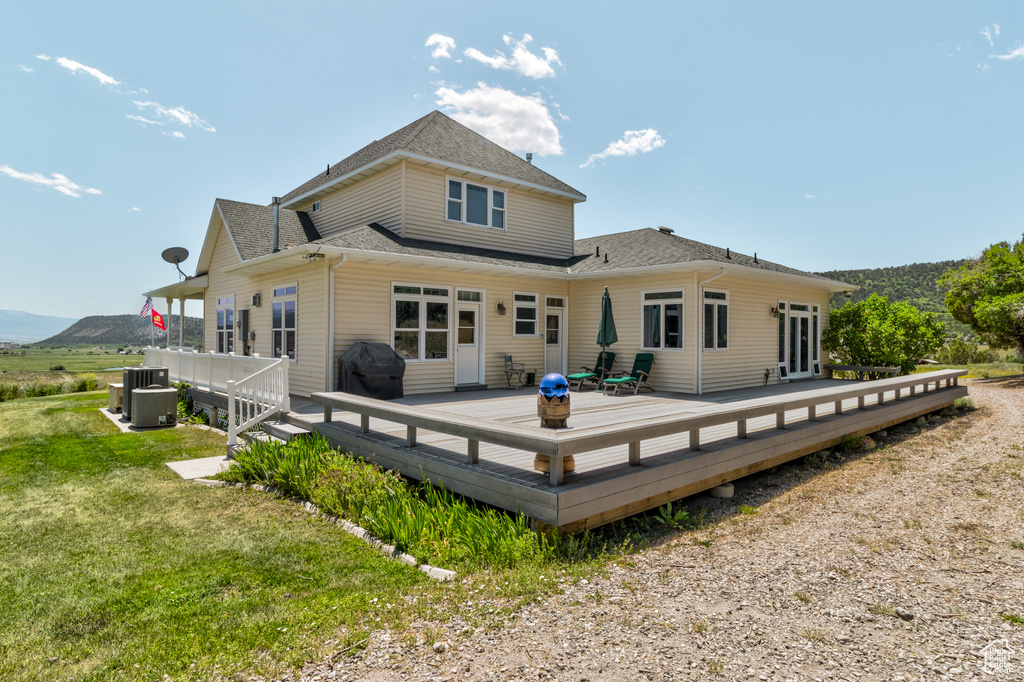Back of house featuring a shingled roof, a wooden deck, and a yard