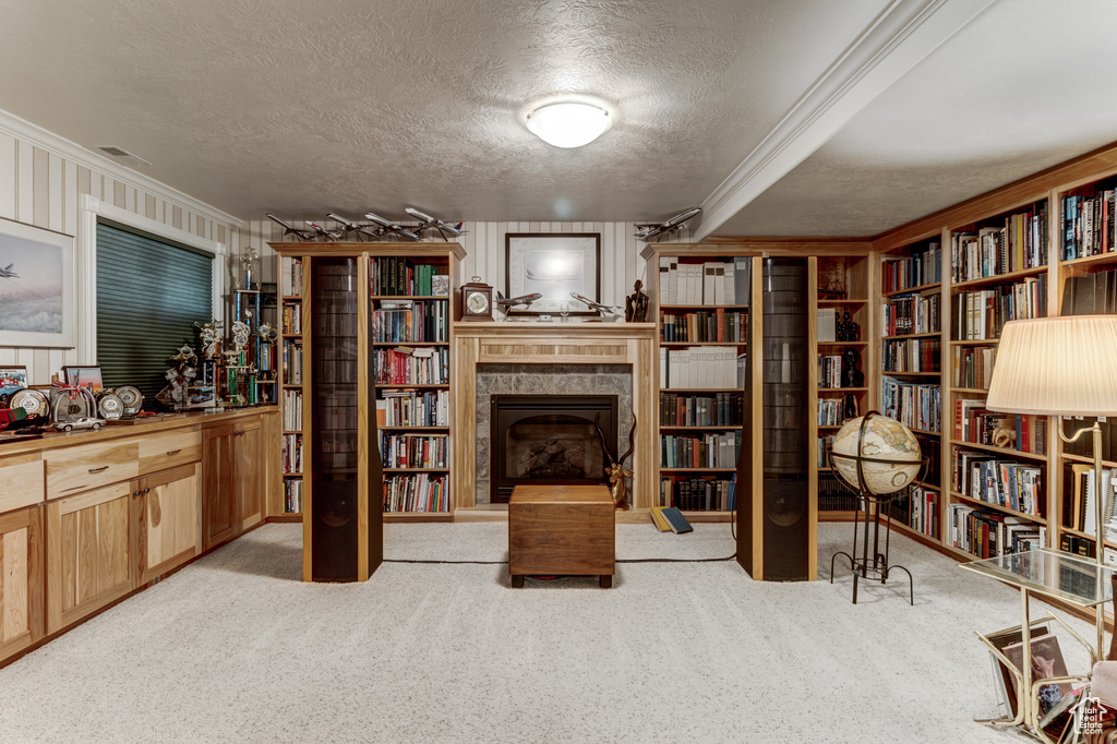 Living area with crown molding, a textured ceiling, carpet, a fireplace with raised hearth, and wall of books