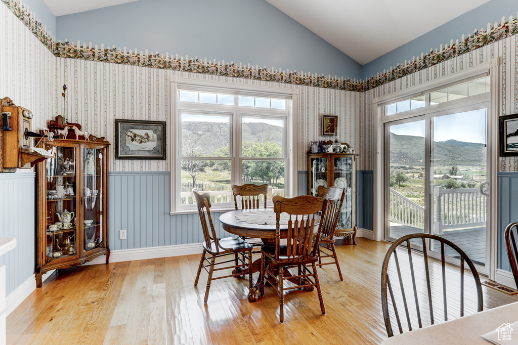 Dining area featuring vaulted ceiling, wallpapered walls, light wood-style flooring, a mountain view, and wainscoting