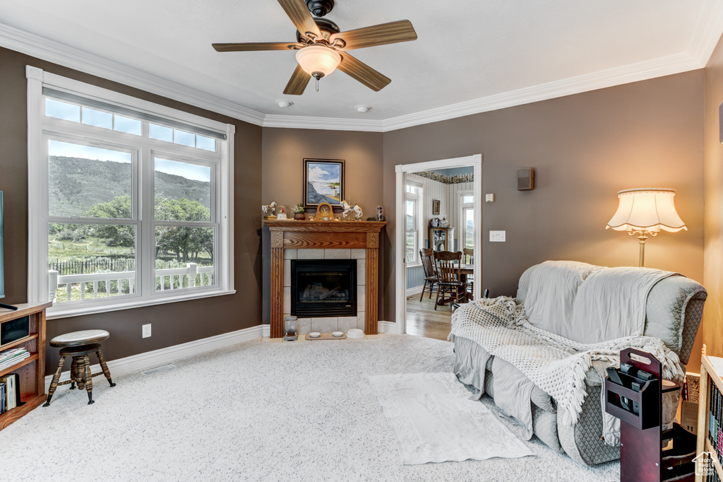 Living area with plenty of natural light, a tile fireplace, ornamental molding, and a ceiling fan