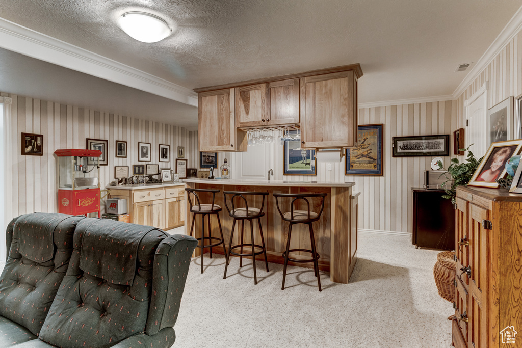Kitchen featuring crown molding, a kitchen bar, light countertops, light colored carpet, and a textured ceiling