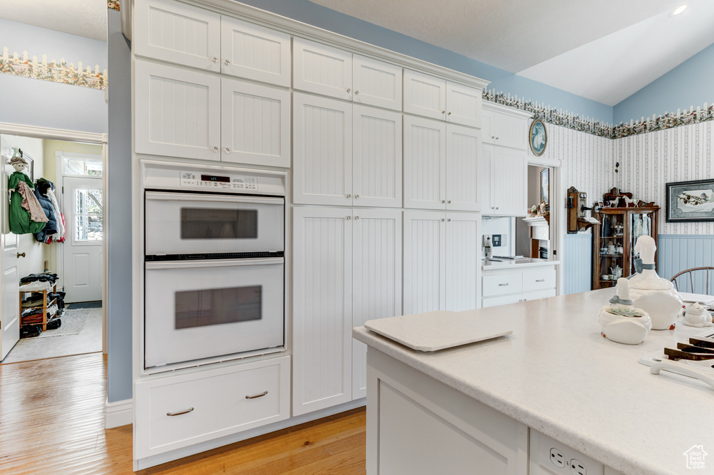 Kitchen featuring white double oven, light wood-style flooring, light countertops, white cabinets, and lofted ceiling