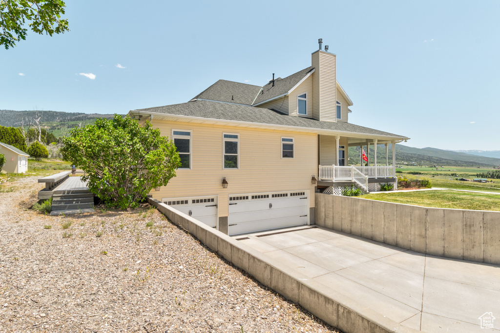 View of side of home featuring concrete driveway, an attached garage, a chimney, covered porch, and roof with shingles