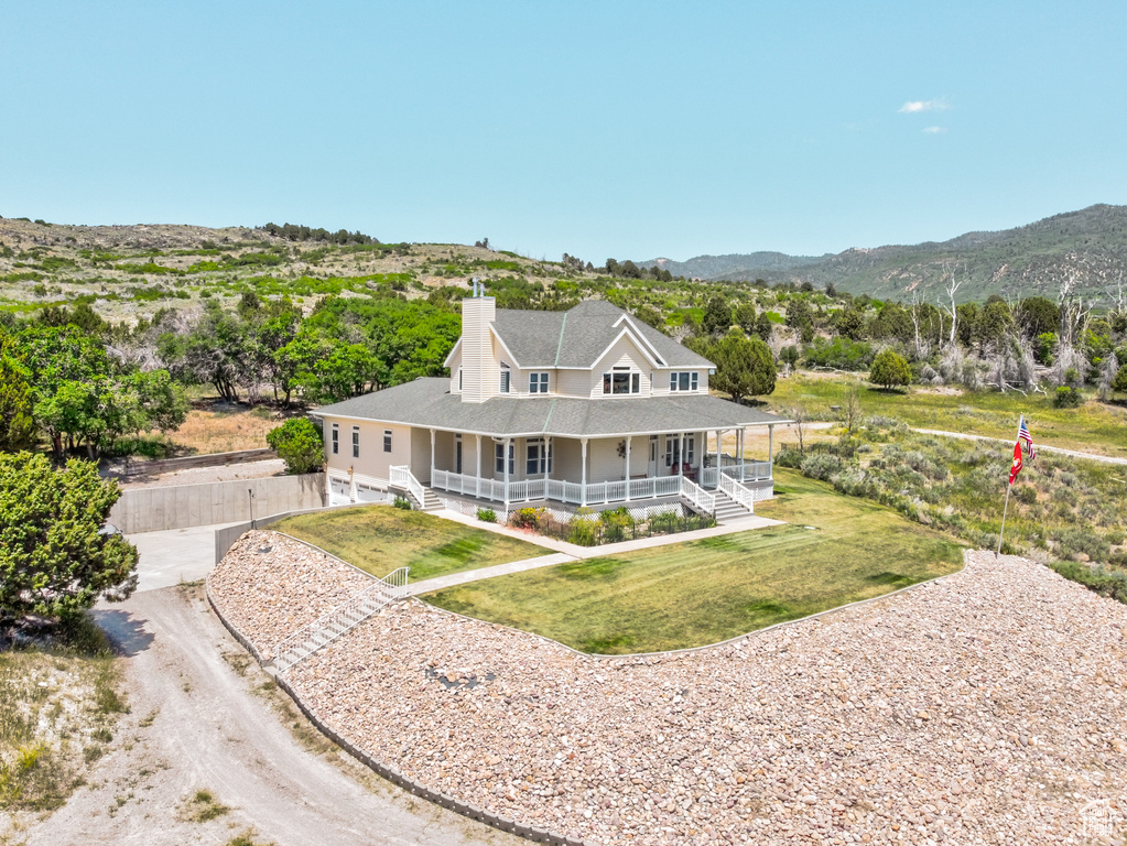 Rear view of property with covered porch, a chimney, roof with shingles, and a mountain view