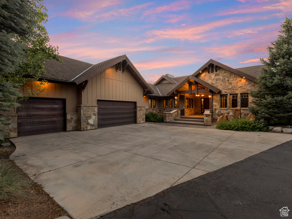View of front facade featuring stone siding, an attached garage, board and batten siding, driveway, and a porch