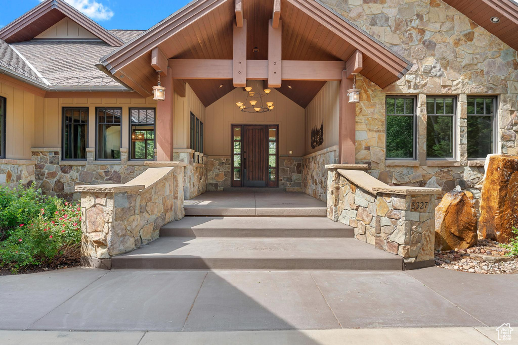 Entrance to property featuring stone siding, roof with shingles, and board and batten siding