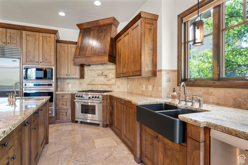 Kitchen featuring built in appliances, premium range hood, tasteful backsplash, light stone counters, and recessed lighting