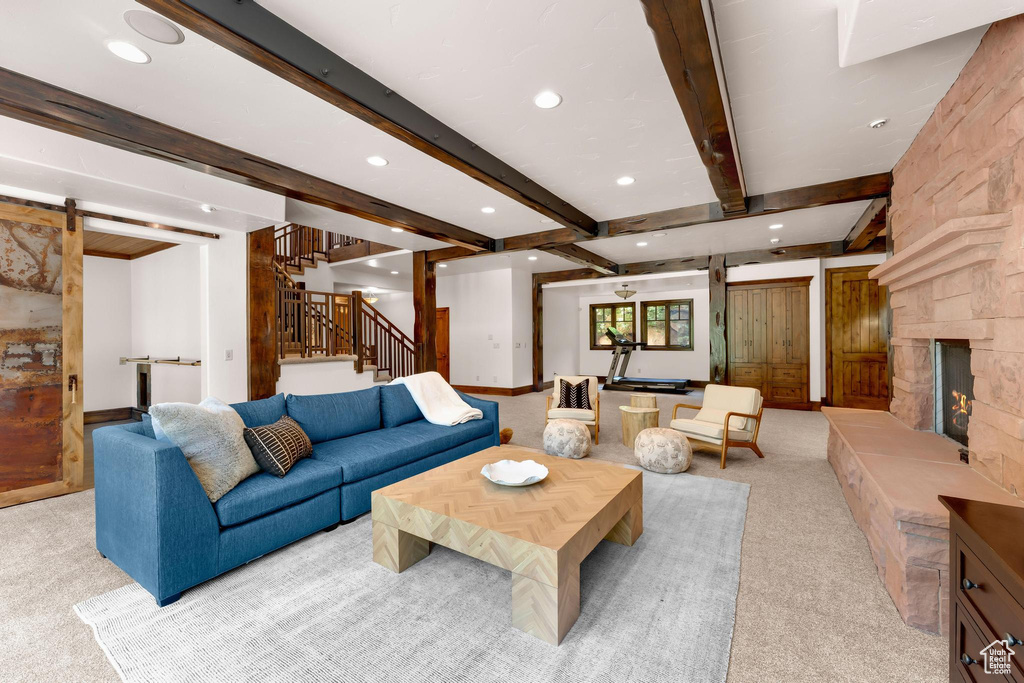 Carpeted living area with recessed lighting, beamed ceiling, stairway, and a stone fireplace