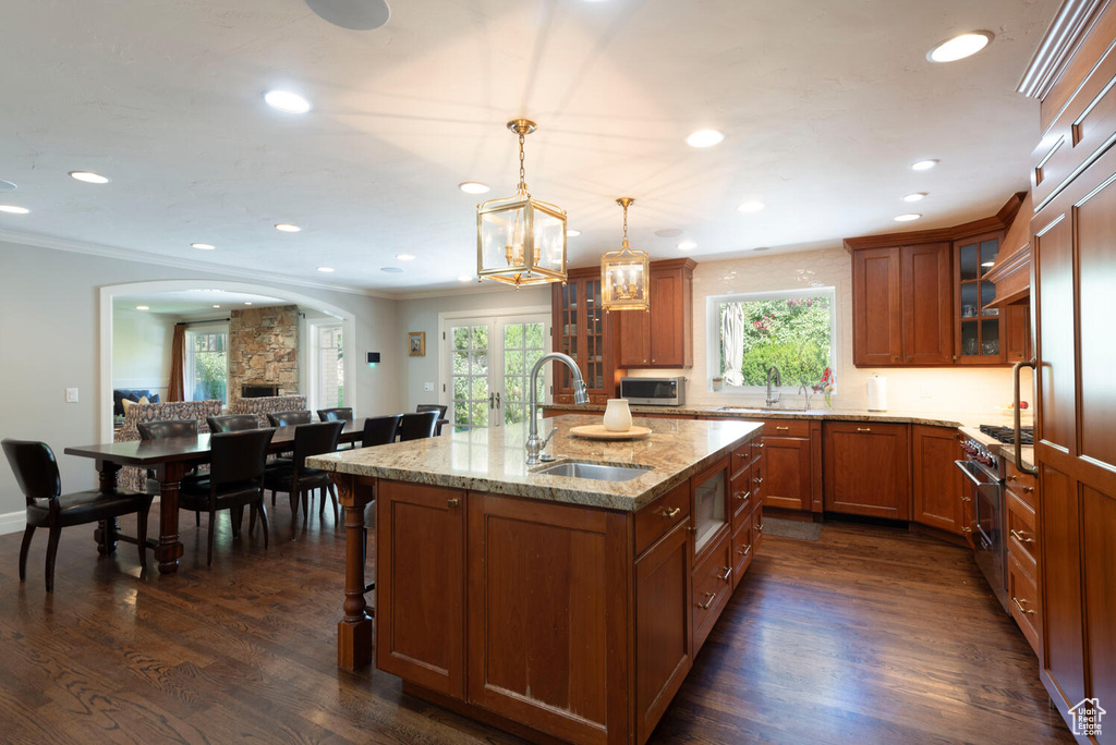 Kitchen with brown cabinetry, appliances with stainless steel finishes, arched walkways, light stone counters, and recessed lighting
