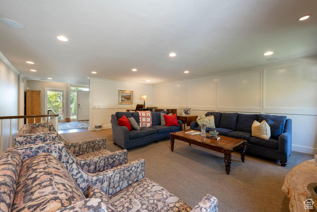 Carpeted living area featuring a decorative wall, ornamental molding, and recessed lighting