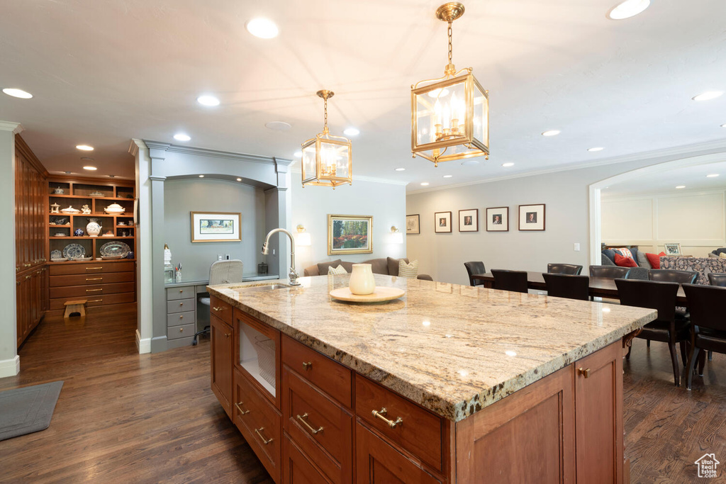 Kitchen with open floor plan, arched walkways, dark wood-type flooring, light stone countertops, and ornamental molding