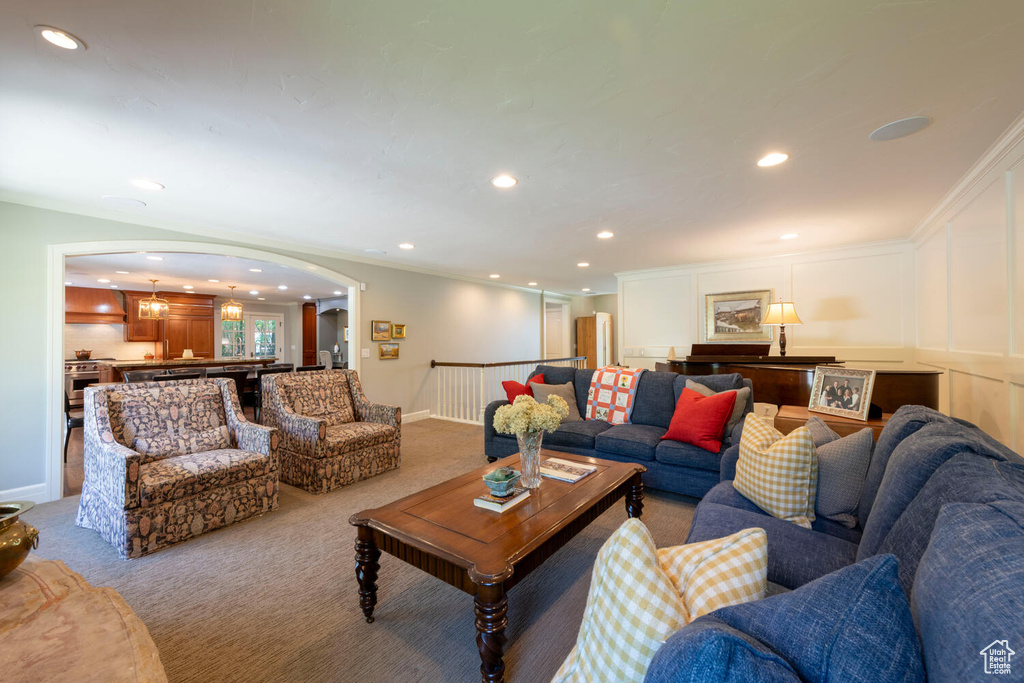 Carpeted living area with arched walkways, recessed lighting, ornamental molding, and ornate columns