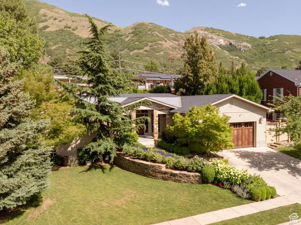 View of front of house featuring concrete driveway, a garage, a mountain view, and a front lawn