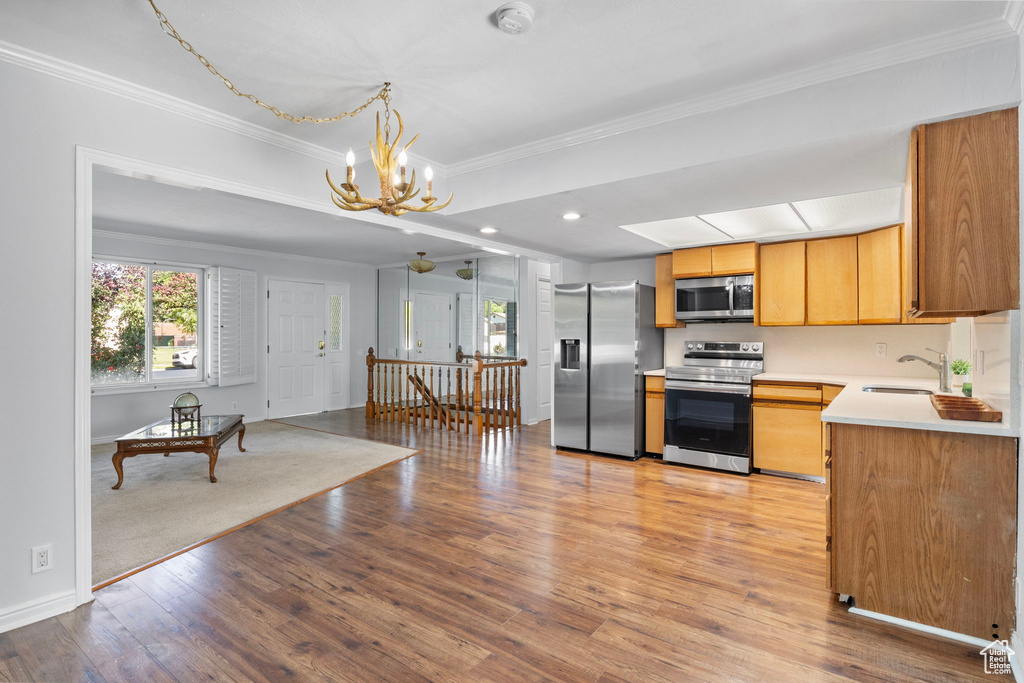Kitchen with appliances with stainless steel finishes, a chandelier, ornamental molding, light countertops, and light wood finished floors
