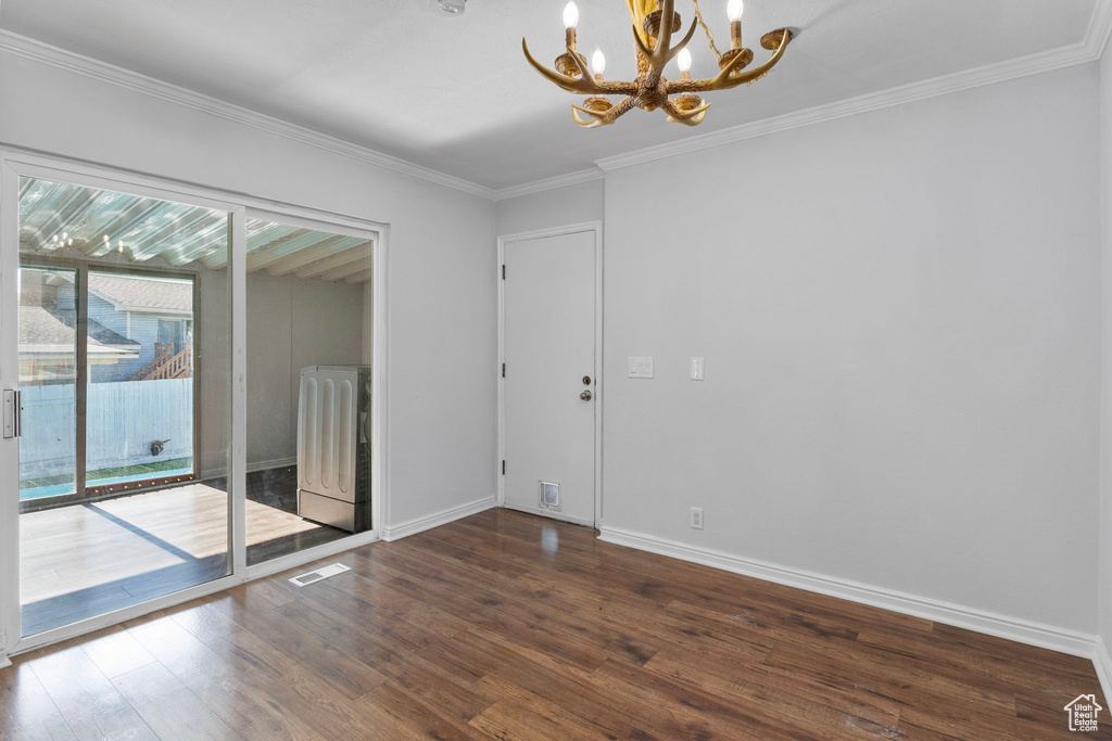 Empty room with a chandelier, wood finished floors, and crown molding