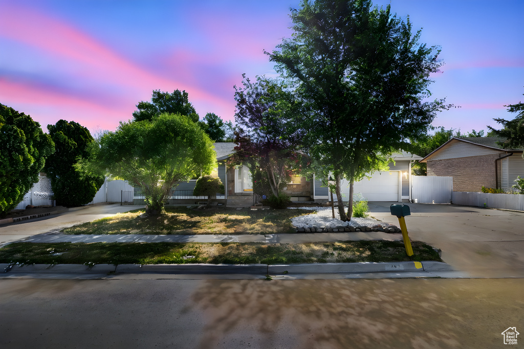 View of property hidden behind natural elements featuring driveway, an attached garage, and brick siding
