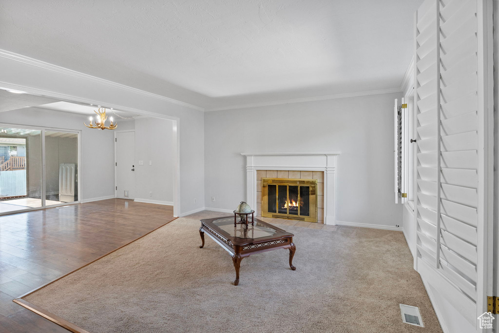 Unfurnished living room featuring a tile fireplace, crown molding, a chandelier, and wood finished floors