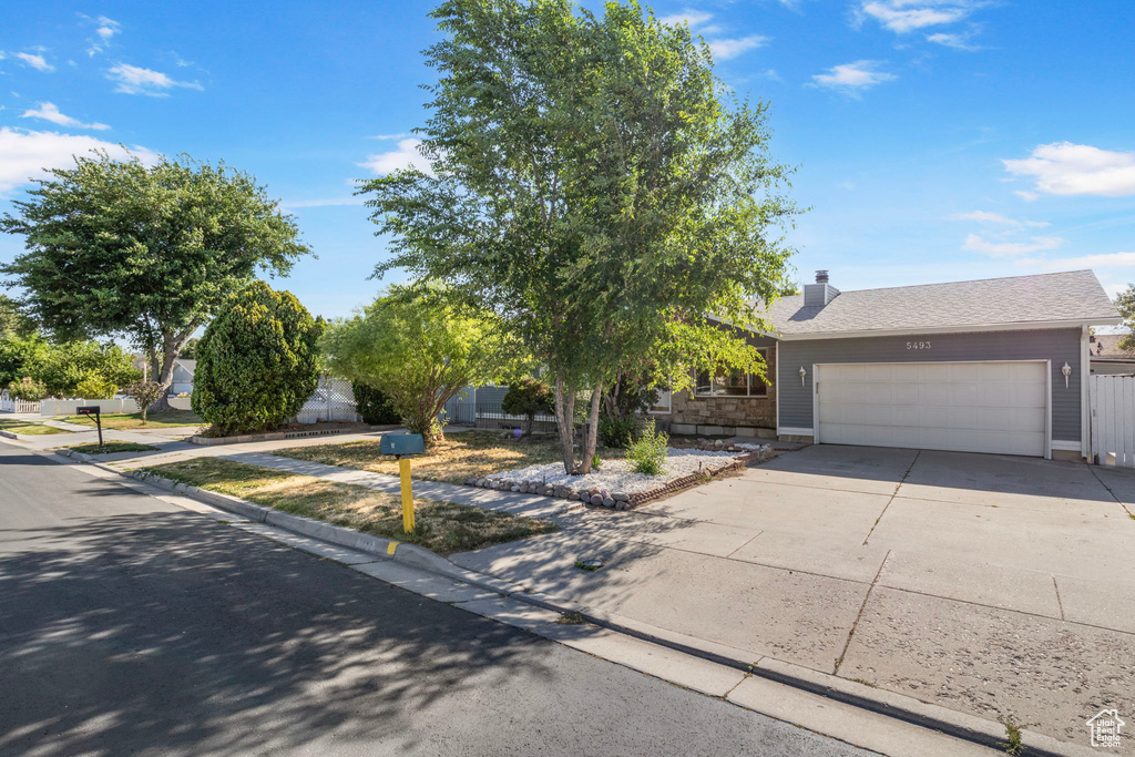 View of property hidden behind natural elements with a garage, driveway, and a chimney